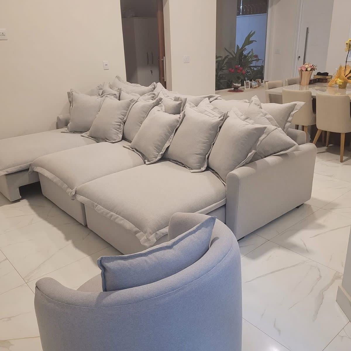 Sofá cinza claro com muitas almofadas e poltrona giratória